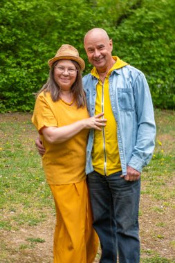 Modern binanın önünde kendine güvenen mutlu, olgun bir çift, sarı şapkalı kadın, ofis binasının yanındaki adam, Avrupa iş mimarisi, kentsel geçmiş. 