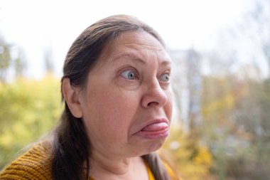 Şok olmuş, şaşırmış olgun bir kadın akıllı telefonunu tutar ve geniş gözleriyle duygusal tepki verir, şok içinde ekrana bakar. Beklenmedik haberlere duygusal tepki, virüs içeriği, beklenmedik online olay 