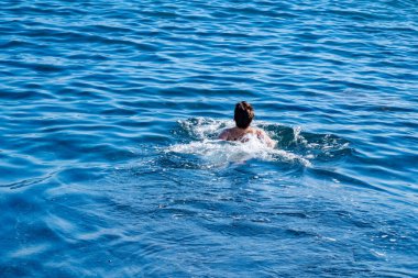 Çocuk denizde neşeyle yüzüyor, yaz tatilinin tadını çıkarırken su güvenliği becerilerini öğreniyor, çocuk deniz dalgalarında oynuyor, kaygısız ve mutlu, ebeveynler güvenliği ve boğulma riskini göze alıyor.
