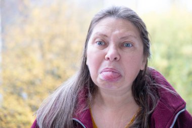 Yakın plan portresi son sınıf öğrencisi bir kadının aptal suratını çıkarması komik bir dil çıkarması komik surat buruşturması yaşlanan mizah kırışıklıkları sonbahar havası, komik yüzlü ve neşeli ruhlu yaşlı bir kadının doğal yakınlığı.