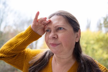 Şaşırmış, orta yaşlı, açık havada uzun saçlı bir kadın, şok olmuş bir yetişkin portresi, stres, hayat sorunları, yüz ifadesi. Şok, şaşkınlık ve beklenmedik duygular konsepti 