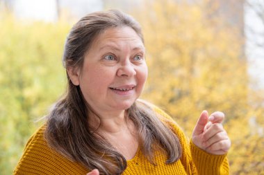 Şaşırmış, orta yaşlı, açık havada uzun saçlı bir kadın, şok olmuş bir yetişkin portresi, stres, hayat sorunları, yüz ifadesi. Şok, şaşkınlık ve beklenmedik duygular konsepti 