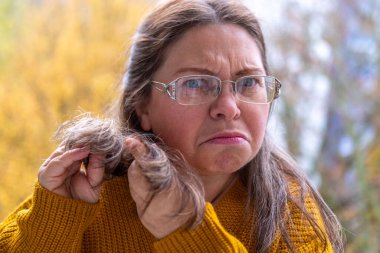 Şaşırmış, orta yaşlı, açık havada uzun saçlı bir kadın, şok olmuş bir yetişkin portresi, stres, hayat sorunları, yüz ifadesi. Şok, şaşkınlık ve beklenmedik duygular konsepti 