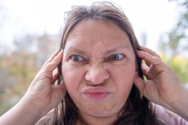 Şaşırmış, orta yaşlı, açık havada uzun saçlı bir kadın, şok olmuş bir yetişkin portresi, stres, hayat sorunları, yüz ifadesi. Şok, şaşkınlık ve beklenmedik duygular konsepti 