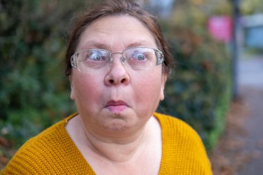 Şaşırmış, orta yaşlı, açık havada uzun saçlı bir kadın, şok olmuş bir yetişkin portresi, stres, hayat sorunları, yüz ifadesi. Şok, şaşkınlık ve beklenmedik duygular konsepti 