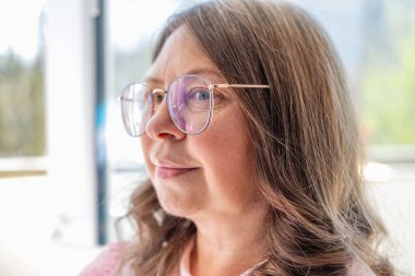 50 yaşında gözlük takan olgun bir kadın, kötü görüş, miyop sorunu, optik muayene, diopter hassasiyeti, gözlüklü bir kadın, doğru lens diopterleri, görüş sağlığı, duygusal portre, yaşlanma