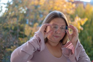 50 yaşında gözlük takan olgun bir kadın, kötü görüş, miyop sorunu, optik muayene, diopter hassasiyeti, gözlüklü bir kadın, doğru lens diopterleri, görüş sağlığı, duygusal portre, yaşlanma