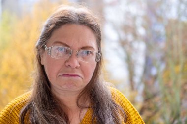 Kuşkucu olgun kadın açık havada, kadın yüzü hayal kırıklığını, şüpheciliği ve duygusal acıyı gösteriyor. Yakın plan, hayal kırıklığını ve şüpheyi gergin bir pozla ifade eden kadın modeli.