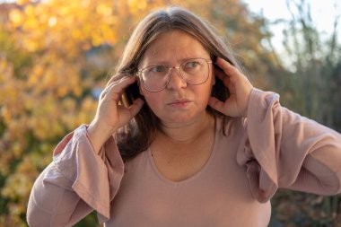 Kulaklarını acılı ifadeyle kaplayan kadın, gürültüden rahatsız olan duygusal portre, çevresel gürültü etkisi portresi, yüksek seslere kendiliğinden tepki, gerçek yüz ifadesi.