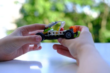 Çocuğun parmakları trafoları manipülatörle hareket ettirir, tasarımcı parçalarından monte edilir, bokeh ile yeşil arka plan, iyi motor becerilerin geliştirilmesi konsepti, yaratıcılık, çocuk eğlencesi 