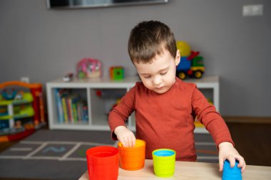 İki yaşında tatlı küçük bir çocuk çocuk çocuk masasında oturuyor ve odasında çok renkli piramitlerle oynuyor. Shildren için eğitici oyuncaklar. Yumuşak seçici odak