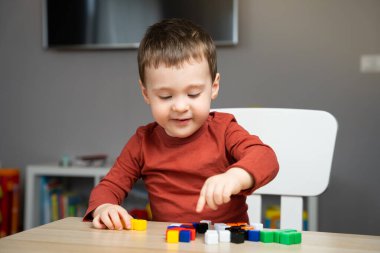 İki yaşında, şirin, mutlu, küçük bir çocuk çocuk bir çocuk masasında oturuyor ve odasında çok renkli bloklarla oynuyor. Çocuklar için eğitici oyuncaklar. Yumuşak seçici odak