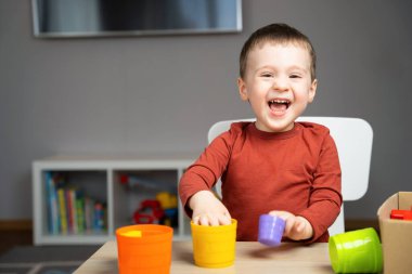 İki yaşında tatlı, mutlu, küçük bir çocuk çocuk bir çocuk masasında oturuyor ve odasında çok renkli piramitlerle oynuyor. Çocuklar için eğitici oyuncaklar. Yumuşak seçici odak