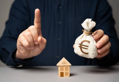 Finansal danışman gayrimenkul satın alma konusunda uyarıyor. Avro para çantasını tutan işaret parmağı olan bir adam. Gayrimenkul almak için en iyi ipotek kredisini seçiyorum. Ev sahibi olmak..