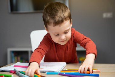 Evdeki çocuk odasında, albümdeki kalemlerle oynayan, iki yıllık mutlu, küçük bir çocuk. Çocuklar için eğitici aktiviteler. Seçici odak.