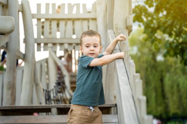 İki ya da üç yıllık şirin, meraklı bir çocuk dışarıda, tahta bir oyun alanında oynuyor. Aktif oyunlar ve çocuklar için eğlence. Yaz günü. Seçici odak
