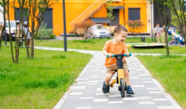 İki ya da üç yaşında tatlı, mutlu bir çocuk güneşli bir yaz gününde bir sitede bisiklet ya da denge bisikleti sürüyor. Dışarıda oynayan aktif bir çocuk..