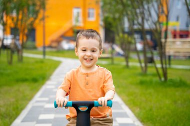 İki ya da üç yaşında tatlı, mutlu bir çocuk güneşli bir yaz gününde bir sitede bisiklet ya da denge bisikleti sürüyor. Dışarıda oynayan aktif bir çocuk. Kapat.