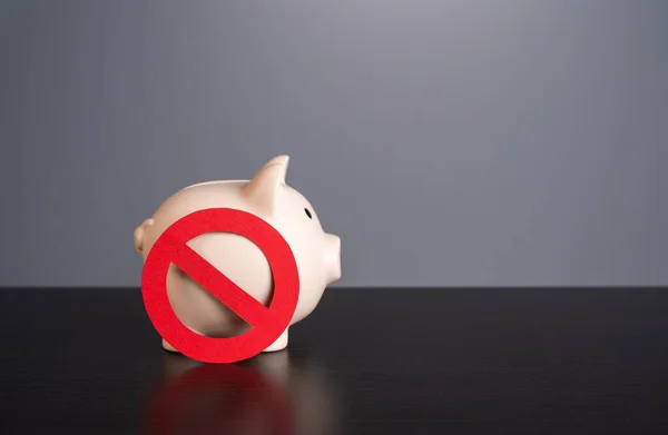 Piggy bank under the symbol of prohibition. Sanctions. Capital outflow restrictions. Freezing savings. Lack of funds. Refusal of savings in favor of investments.