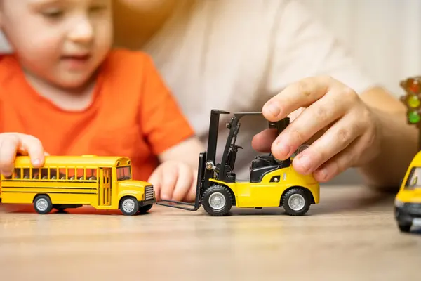 Father and son play with cars. Spending time with children. The concept of a happy childhood. School bus and forklift. Close up. Focus on the toy car.
