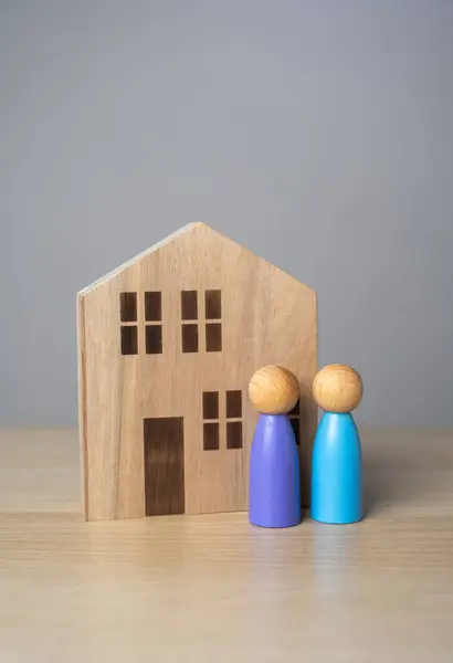 People and house figurines. The owners are standing near the house. Buying and selling real estate. Housing prices. Finding the best home to buy. Affordable housing for families and young.