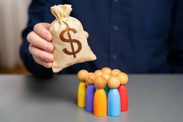stock image Businessman holding dollar money bag over group of people figurines. Allocation of budget money for social projects. Preferential loans for entrepreneurs and businesses. Social support, assistance.