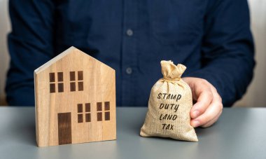 Stamp duty land tax SDLT concept. Taxes assessed during the transfer of real estate between two parties. Buying housing and land. Money bag in the hands of a businessman and a miniature house clipart