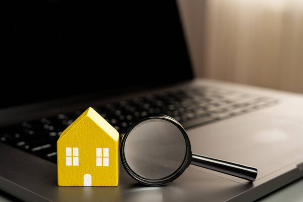 House and magnifying glass on laptop keyboard. The concept of searching for housing via the Internet. Find an apartment for rent online. Property valuation and realtor services