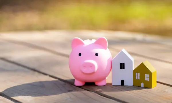Wooden houses and piggy bank stands outdoors on a sunny day. Real estate and investments in housing concept. Mortgage, loan. Eco-friendly house