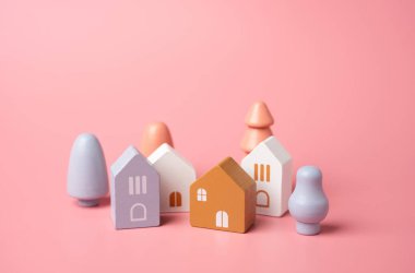 Pembe arka planda figürlerden oluşan şirin bir kasaba. Tahta oyuncaklar. Bir ev al. Güzel bir ev. İpotek. Pastel pembe renkler.