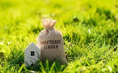 Mortgage tefecisi para çantası ve çimenlikte bir ev. Konut kredisi sunan ve sigortalayan finans kurumu veya mortgage bankası. Para ve gayrimenkul finans kavramı.
