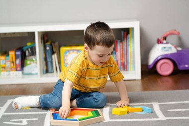 Bandajlı ya da bacağında alçı olan küçük çocuk tahta bloklarla oynuyor. Çocuklarda ayak ve parmak kırığı. İnsan sağlığı ve tıp konsepti