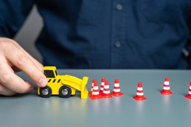 A man removes traffic cones with a bulldozer. The concept of lifting restrictions and prohibitions. Revocation of sanctions and termination of embargo. Termination of seizure and freezing of funds. clipart