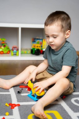 2,5 yaşında küçük bir çocuk oyuncak bir helikopterle oynuyor, onu monte ediyor ve parçalara ayırıyor. Çocuklar için eğitici oyuncaklar. Evde çocuk odası var. Kapalı