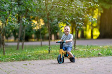 Güneşli bir yaz gününde, üç ya da dört yaşında tatlı, gülümseyen bir çocuk bisiklet ya da denge bisikleti sürüyor. Bebeklik ve çocukluk kavramı. Seçici odak
