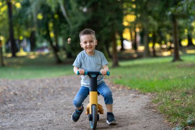Güneşli bir yaz gününde, üç ya da dört yaşında tatlı, gülümseyen bir çocuk bisiklet ya da denge bisikleti sürüyor. Bebeklik ve çocukluk kavramı. Seçici odak