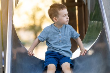 Üç buçuk yaşında beyaz, tatlı bir çocuk bir yaz günü oyun parkında kaydırağın altına iniyor. Dışarıda oynayan aktif bir çocuk. Çocukluk kavramı.