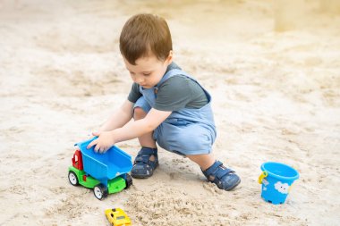 2.5 yaşındaki küçük tatlı çocuk güneşli bir yaz gününde kum havuzunda oynuyor. Çocuklar için açık havada yaratıcı aktiviteler. Oyuncak araba ve kürek..