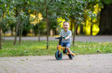 Güneşli bir yaz gününde, üç ya da dört yaşında tatlı, gülümseyen bir çocuk bisiklet ya da denge bisikleti sürüyor. Bebeklik ve çocukluk kavramı. Seçici odak