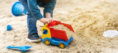 Küçük tatlı çocuk üç yaşında bir bahar günü kum havuzunda oynuyor. Çocuklar için açık hava gelişim aktiviteleri. Oyuncak arabalar ve kürek. Arabaya odaklan.