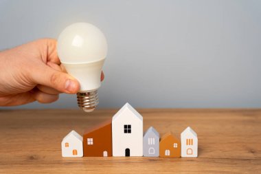 Konut binalarına el ele tutuşan ampuller. Güç kaynağı kavramı. Akıllı evlerin yenilikleri ve teknolojileri. Özerk enerji ve barınma. Enerji tasarrufu.