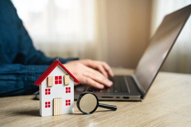 İnternet üzerinden konut arama kavramı. İnternetten kiralık bir daire bul. Emlak fiyatları ve emlakçılık hizmetleri. Ev, büyüteç ve dizüstü bilgisayarı olan adam..