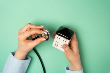 Küçük evin yakınında steteskop tutan bir kadın. Konut durumu ve bakım. Daire tadilatı. Mülk değeri. Emlak kavramı