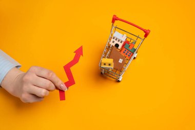 Gayrimenkul, inşaat oranları ve eğilimlerde artan talep. Artan konut fiyatları. Kiralık. Evleri olan bir süpermarket arabası ve kadınların elinde bir ok..