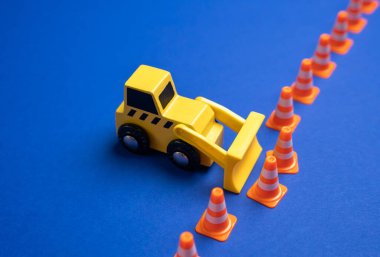 Bir buldozer trafik konilerinden yapılmış bir sınır çitini itiyor. Kurallardan feragat. Anlaşmaları bozmak. Yönetmelikleri gözden geçirmek ya da sınırları zorlamak. Normallerin bozulması.
