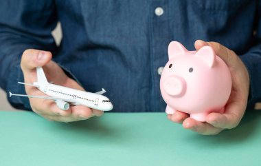 Bir adam bir uçak ve kumbara tutuyor. Seyahat birikimleri. Bütçe uçuşları. Ucuz biletler. Maliyet optimizasyonu. Tatil planlama. Bütçesi kısıtlı turizm.