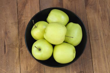 Many green apples in a black round plate on a wooden background