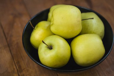 Many green apples in a black round plate on a wooden background