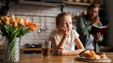 Üzgün çocuk tatlı çöreklerin yanında oturuyor ve meyve suyu evde yoğun bir ebeveyn, ezilmiş ebeveyn konsepti.