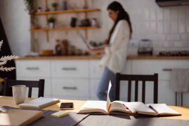 Akıllı telefon ve kitaplar evdeki mutfakta dizüstü bilgisayarı olan bulanık bir kadının yanındaki masada. 